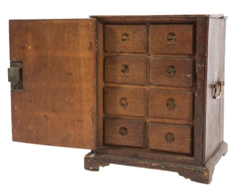 An 18th Century oak spice cabinet:, fitted with eight small drawers, enclosed by a panel door, having brass carrying handles 