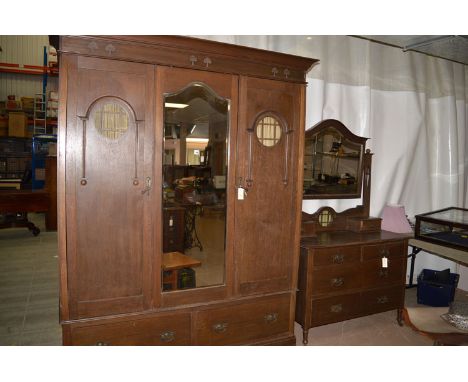 An Arts and Crafts wardrobe with centre mirror panel flanked by doors and drawers to base; with matching dressing table.