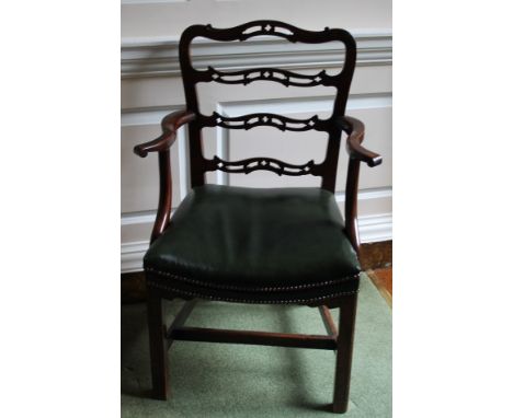 A George III mahogany open arm chair, with a pierced ladder back, scrolling arms and a green leather padded seat with studded