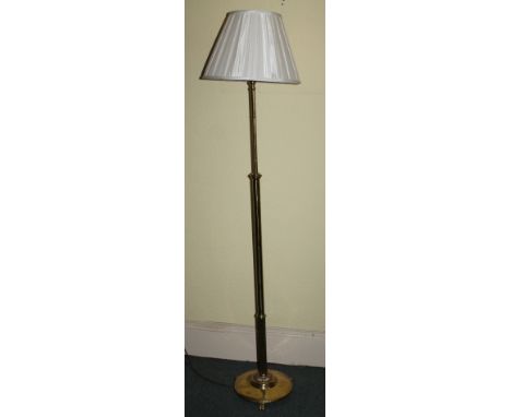 An early 20thC brass floor lamp, of cylindrical form on a circular base with three moulded feet, and a shade, 175cm high.