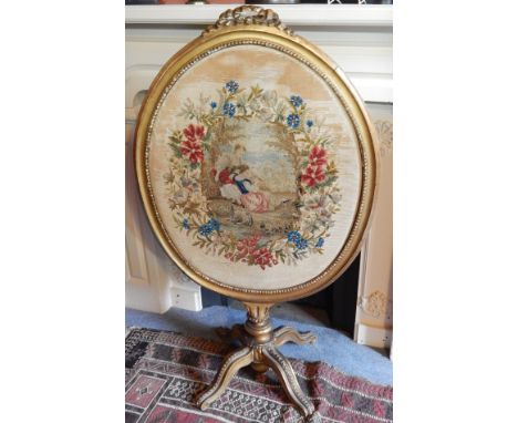 A 19thC giltwood and gesso fire screen, the oval beaded frame inset with a woolwork panel depicting figures within a floral c