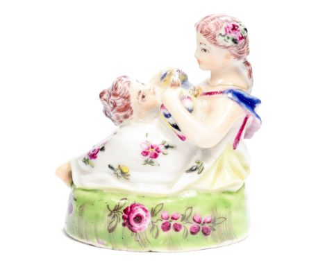 A porcelain snuff box cover moulded as a lady with a child holding two doves and sitting on a grassy mound, possibly a copy o