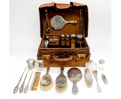 A George V crocodile skin travelling toilet case, fitted with silver topped glass bottles and brushes, engine turned stripe d