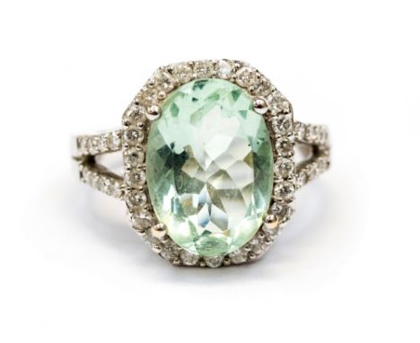 A diamond and aquamarine oval cluster white gold cocktail ring with diamond set split shoulders, the oval mixed cut aquamarin