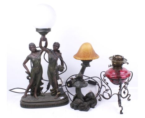 A cranberry oil lamp and two electric lamps. The oil lamp with a scrolling metal frame, H30cm, one of the electric lamps with
