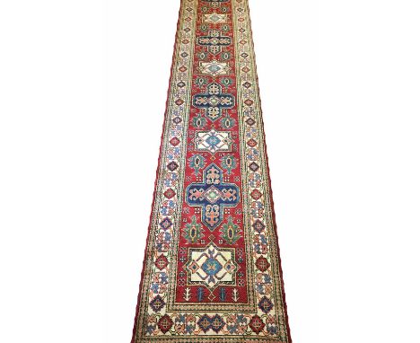 FINE KAZAK RUNNER, 464cm x 85cm, of multiple medallions on ruby field within ivory borders.