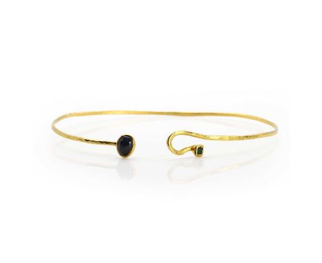 A sapphire and emerald gold bangle, a fine wire work bangle, with a hammered finish, one end set with a blue sapphire in a ru