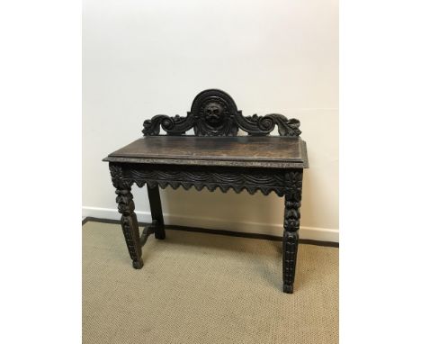 A Victorian carved oak Gothic Revival side table, the raised back with grotesque mask or sunburst decoration over a guilloche