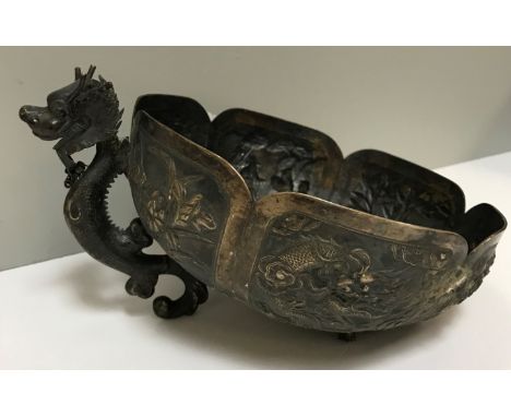 An Oriental white metal bowl with embossed dragon and foliate decoration and dragon foot (two others missing), bears stamp to