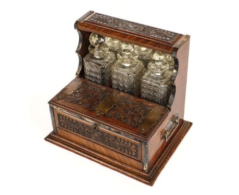 * Tantalus. A Victorian oak tantalus, with carved panels and plated mounts, holding three square-cut glass decanters each wit