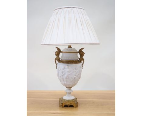 An Empire period biscuit porcelain urn with bas relief and solid brass mounts, as a table lamp, and with cream pleated shade,