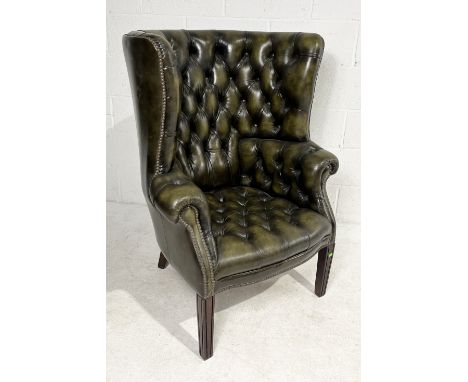 A leather Chesterfield armchair raised on mahogany square tapering legs and having a tall and deep rounded wingback frame uph