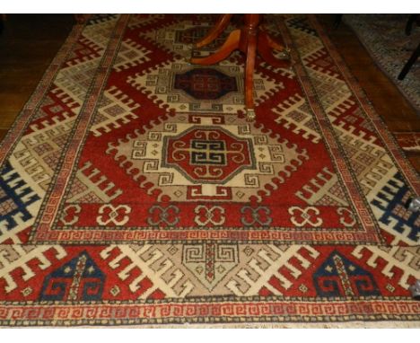 A red ground Kazak carpet, having three geometric shaped medallions to centre, multi-bordered and fringed, L.295cm, W.208cm