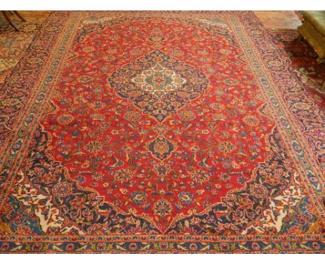 A Kashan burgundy ground carpet woven central lobed floral medallion within scattered floral field and wide conformity border