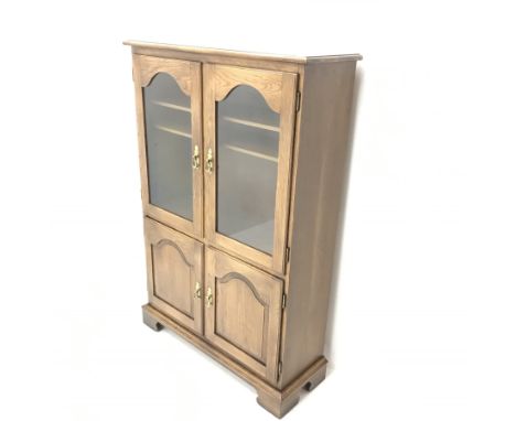 Jaycee - medium oak display cabinet, two glazed doors enclosing two shelves above two panelled cupboards, shaped bracket supp