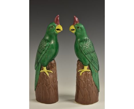 A pair of Chinese models of parrots, in the Kangxi taste, each perced upon a trunk, glazed in tones of green, brown, yellow a