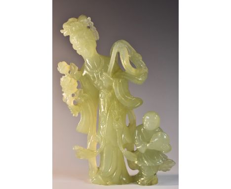 A Chinese jade figure, carved as Guanyin, she stands, holding blossom and a whisk, a young boy at her side, 23cm high