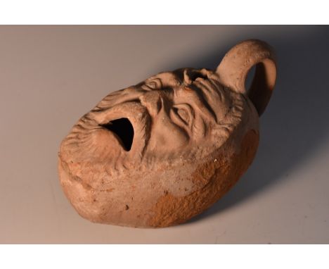 A terracotta oil lamp, modelled with a face, his mouth agape, scroll handle, 15cm long