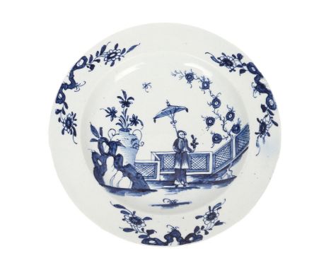 A LOWESTOFT PORCELAIN PLATE. circa 1770, the body underglaze blue decorated with a lady holding a parasol in a garden with fe