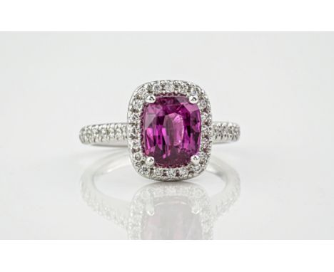 An 18ct cushion cut pink sapphire and diamond cluster ring, the central pink sapphire weighing approximately 3.10ct and surro