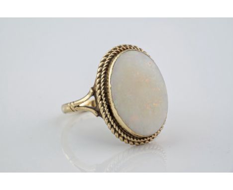 A large 9ct yellow gold and opal ring, featuring an oval cut opal of 18mm in length and in a rubover setting with rope detail