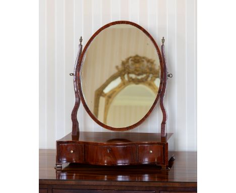 A George III mahogany serpentine box base toilet mirror, the oval plate on shaped uprights, over a three drawer base with bar