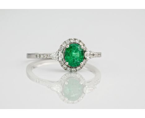 An 18ct white gold, diamond and emerald ring., With the central oval cut emerald surrounded by a diamond halo, with 2 pear cu