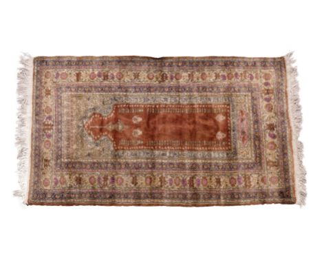 A Ghiordes prayer rug, the copper red field below a buff mihrab with purple, light brown and pink Arabic calligraphy to borde