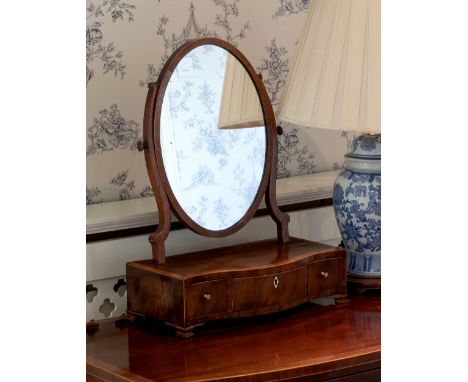 A George III mahogany serpentine box base toilet mirror, the oval plate over a tulipwood cross banded base with three drawers