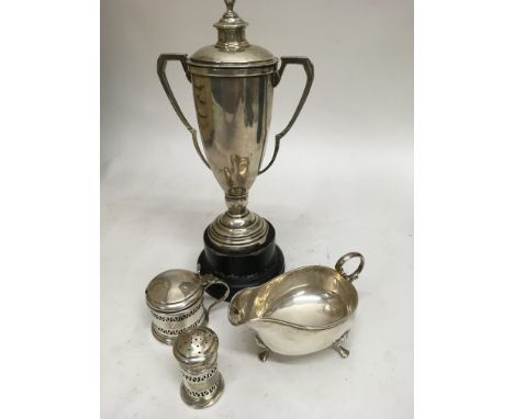 A silver trophy cup together with milk jug and condiments.