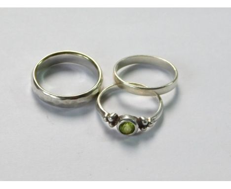 SILVER RINGS. Two silver dress rings: a plain silver band & a peridot-set dress ring. Sizes J & J/K. Also, a contemporary sil