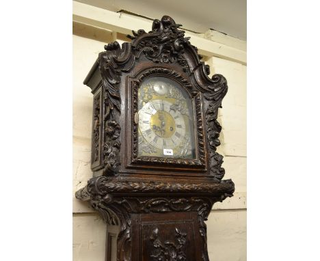 Late 18th or early 19th Century continental carved oak longcase clock, the arched hood with carved surmount above a panel doo