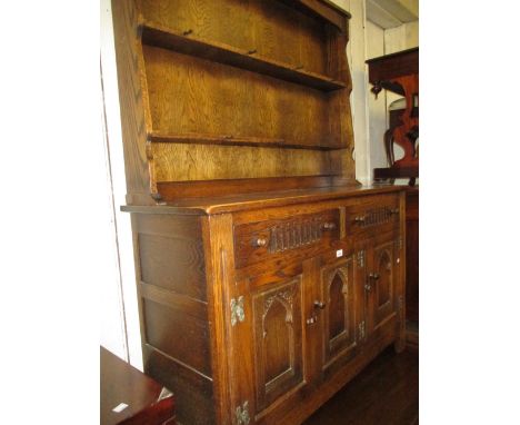 Small reproduction oak dresser with boarded shelf back above two drawers and two arched cupboard doors on stile supports