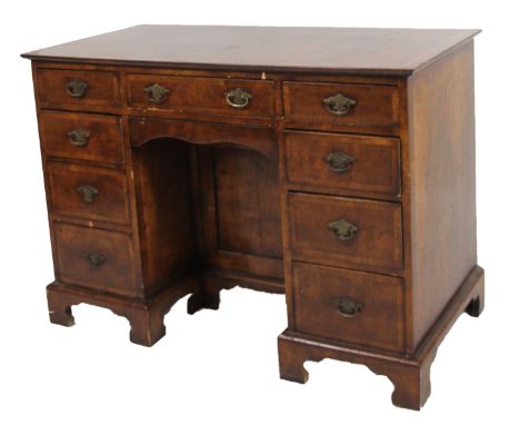 A George I style walnut kneehole desk, the overhanging wide crossbanding top raised above three frieze drawers and six pedest