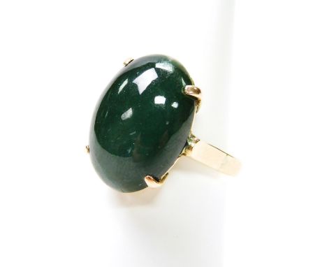 A jade dress ring, with oval green jade in claw setting, on a yellow metal band, in worked frame, yellow metal, marked 14K, 5