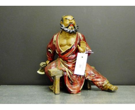 A Japanese red glazed figure of an axe man, modelled seated on a trestle stool, 28cm high 