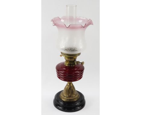 An early 20thC brass oil lamp, embossed with leaves, with a ruby glass reservoir and black base, the shade etched with flower