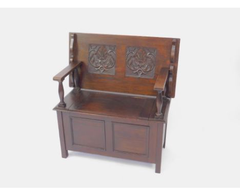 An early 20thC oak monk's bench, with a carved panel back decorated with acanthus leaves, over a trunk base with lift up lid,
