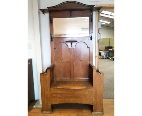 A late 19th/early 20th century oak Arts and Crafts hall stand/seat with curved pediment cresting over a fielded back pane set