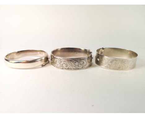 Three silver bangles to include; A silver buckle bangle, A silver half engraved bangle, A silver half engraved bangle (dented