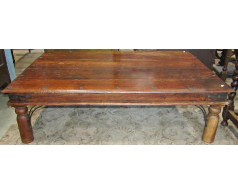 A low Indian hardwood occasional table of rectangular form with metal fittings raised on simple turned supports 135 cm long x