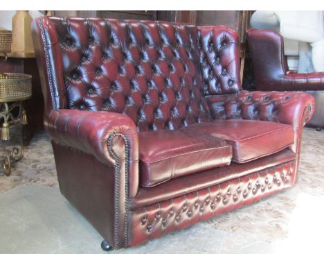 A small button back wing sofa and two matching chair together with a foot stool, all in oxblood coloured leather style finish