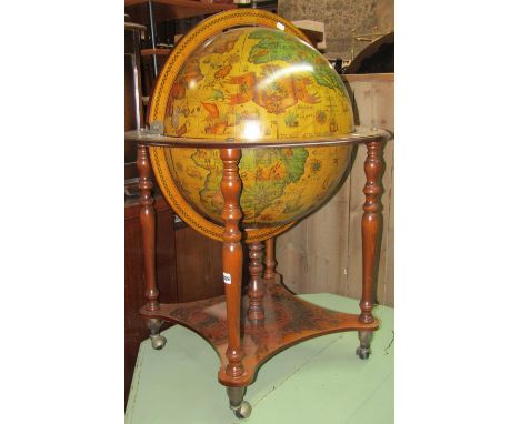 A drinks cabinet in the form of a reproduction terrestrial globe and stand with stained beechwood supports and set on castors