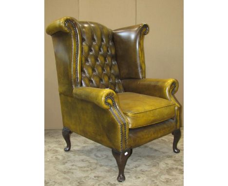 A button back wing chair in the Georgian style with scrolled arms on short cabriole supports, upholstered in buttoned leather