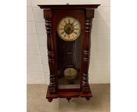 A mahogany wall clock with turned pillars to case and glazed door opening to reveal clock face (H107cm W45cm D19cm)