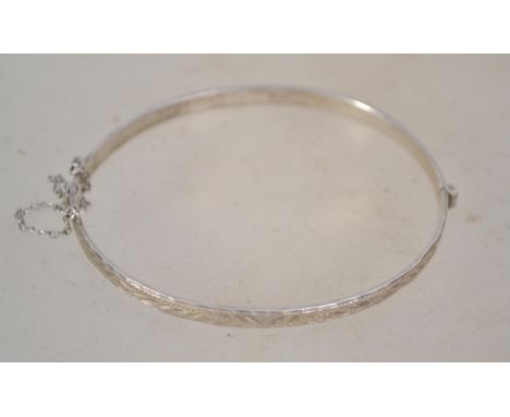 A hallmarked silver bangle bracelet having a half engraved design and safety chain. Weighs 8.1 grams and measures 7cms wide.