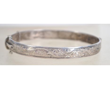 A hallmarked silver bangle bracelet, having half engraved foliate design with safety chain. Hallmarked for Birmingham 1960. M