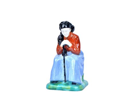 A Gmunder Keramik Austrian pottery figure, circa 1930, modelled as an old woman, seated and hunched over her walking stick, m