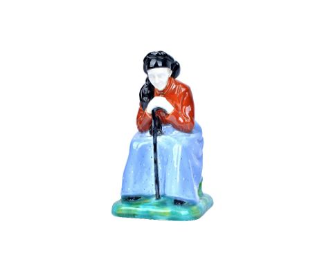 A Gmunder Keramik Austrian pottery figure, circa 1930, modelled as an old woman, seated and hunched over her walking stick, m