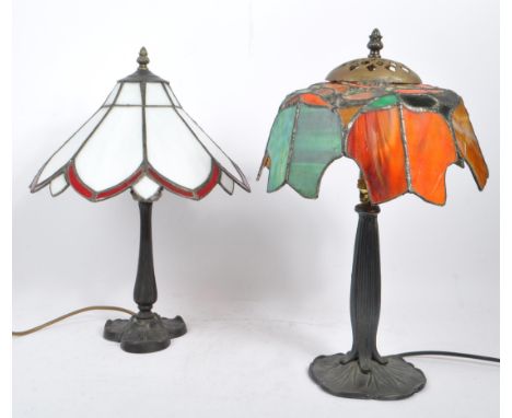 Two 20th century Tiffany manner desk / table lamps. Each lamp having cast spelter bases, having foliate design feet. One lamp